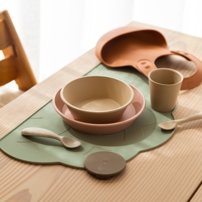 Conjunto de alimentação infantil com prato, tigela, copo e colheres em mesa de madeira