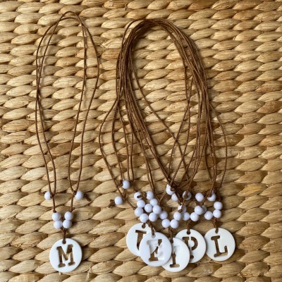 Colares com pendentes redondos brancos com letras secas castanhas em cordões castanhos sobre tecido trançado