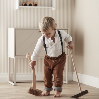 Criança pequena a brincar com vassoura e pá em ambiente interior claro