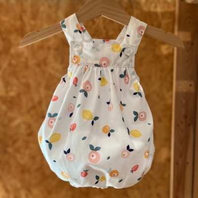 Macacão curto de bebé com padrão de frutas coloridas pendurado num cabide de madeira