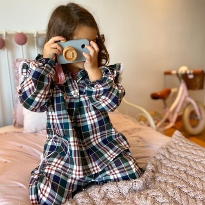 Camisola xadrez de criança sentada numa cama com manta e bicicleta ao fundo
