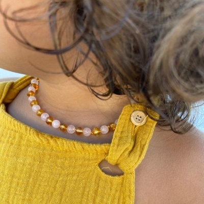 Colar de contas rosa e âmbar em criança com vestido amarelo e botão de madeira