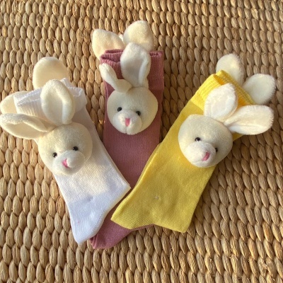 Três pares de meias com cabeças de coelho de pelúcia em branco, rosa e amarelo
