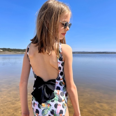 Fato de banho infantil estampado com pássaros e laço preto nas costas em ambiente de lago