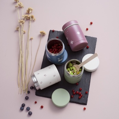 Três frascos coloridos com frutas e legumes, sobre placa preta e flores secas