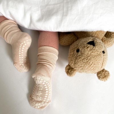 Meias antiderrapantes creme para bebé em cama branca com peluche castanho