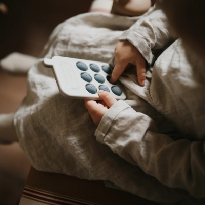 Criança com roupa clara segurando brinquedo educativo branco com botões cinza