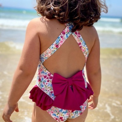 Fato de banho infantil floral com laço vermelho e folhos visto de costas na praia