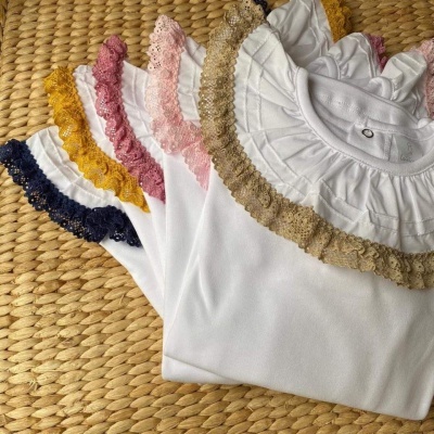 Camisas brancas com golas em renda colorida sobre superfície de palha