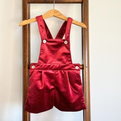 Jardineira infantil de veludo vermelha pendurada num cabide numa escada de madeira.