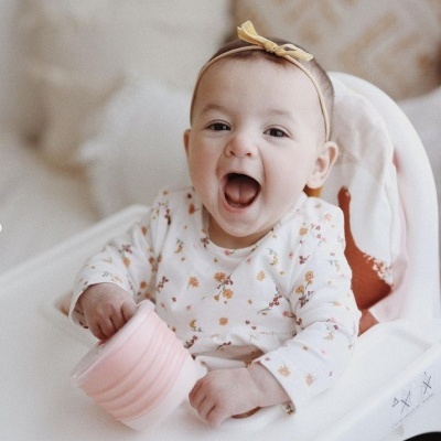 Bebé sorridente na cadeira alta com copo rosa e body floral.