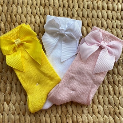 Três pares de meias de bebé coloridas com grandes laços, sobre superfície trançada