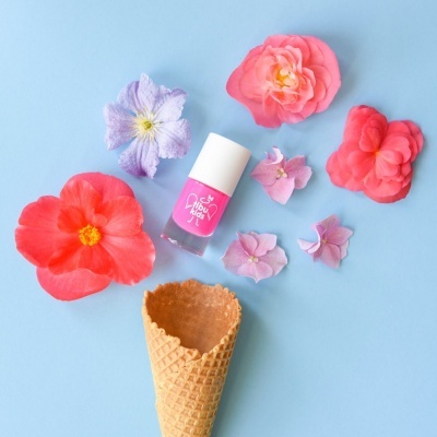 Frasco de verniz para unhas rosa com flores coloridas e casquinha de gelado sobre fundo azul
