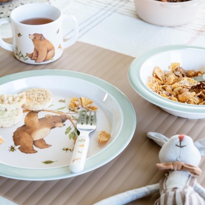 Conjunto de loiça infantil com ursos e abelhas, copo, prato, tigela, garfo e peluche de coelho sobre mesa