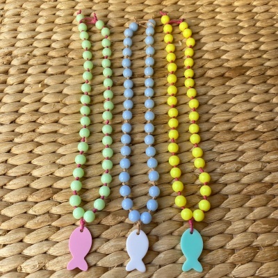 Três colares coloridos com pingentes de peixe sobre tapete de palha