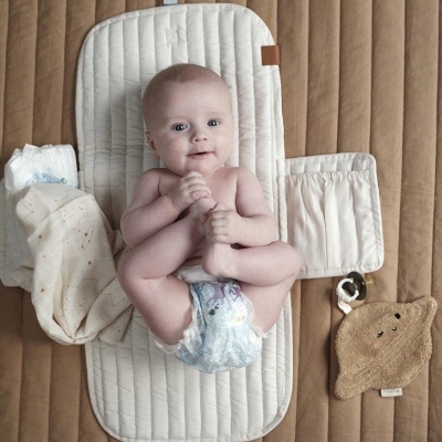 Bebé com fralda numa almofada branca acolchoada, manta e brinquedo de peluche em forma de estrela castanha.