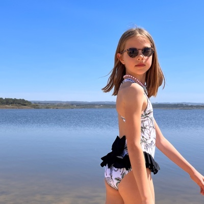 Jovem com fato de banho floral branco e preto, óculos de sol, junto a um lago