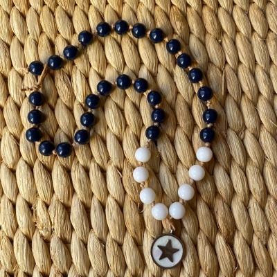 Colar azul e branco com pendente de estrela sobre tecido trançado bege
