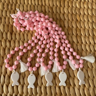 Colares com contas rosa e pendente de peixe branco sobre superfície trançada castanha