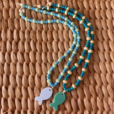 Colares coloridos com pendentes em forma de peixe sobre superfície trançada.
