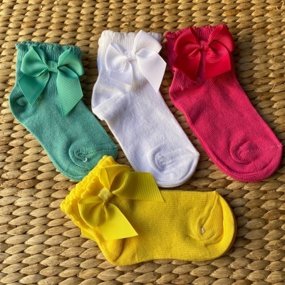 Quatro pares de meias infantis coloridas com laços sobre fundo de tecido de palha