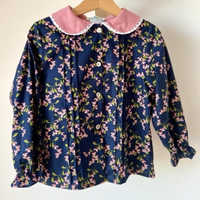 Blusa infantil floral azul escuro com gola rosa pendurada num cabide.