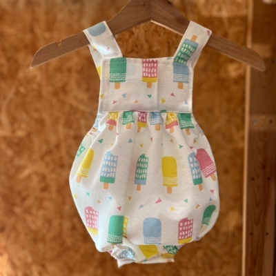 Body de bebé branco com padrão colorido de gelados pendurado num cabide de madeira