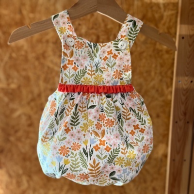 Vestido bebé floral com cinto vermelho pendurado num cabide de madeira