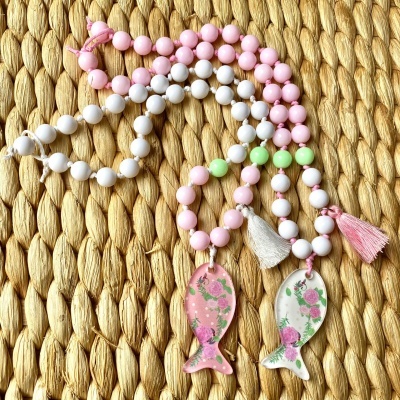 Colares coloridos com pingentes em forma de peixe e contas redondas sobre fundo de juta