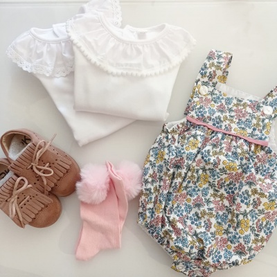 Roupa de bebé com body branco, mocassins castanhos, meias cor-de-rosa e jardineira floral.