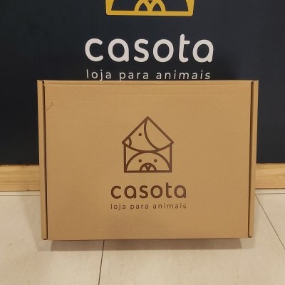 Caixa de cartão com logotipo e texto Casota loja para animais em frente a parede preta com o mesmo logotipo