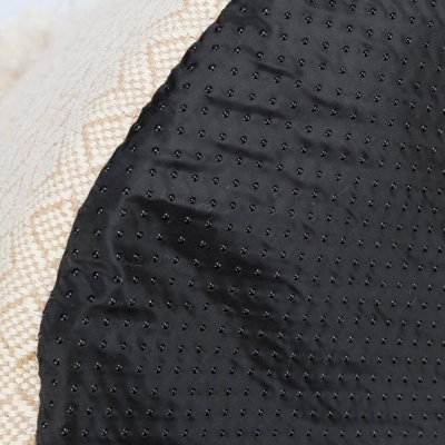 Almofada redonda preta com textura sobre superfície bege com padrão geométrico