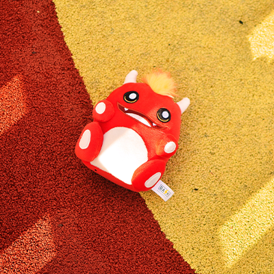 Carteira vermelha de desenho animado com olhos grandes e chifres sobre superfície amarela e vermelha texturada