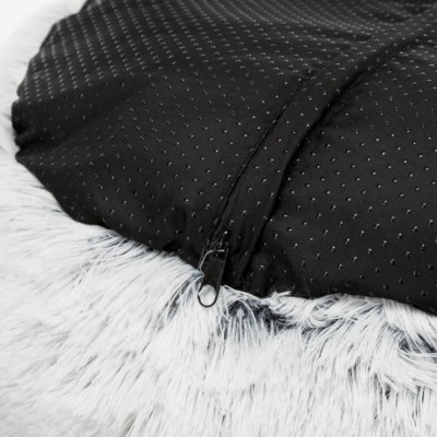 Bolsa preta com textura de pontos e zíper sobre pelo sintético branco.