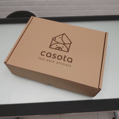Caixa de cartão castanha com logo e texto 'casota loja para animais' sobre mesa branca