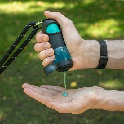 Frasco dispensador portátil com líquido azul a ser aplicado na mão ao ar livre