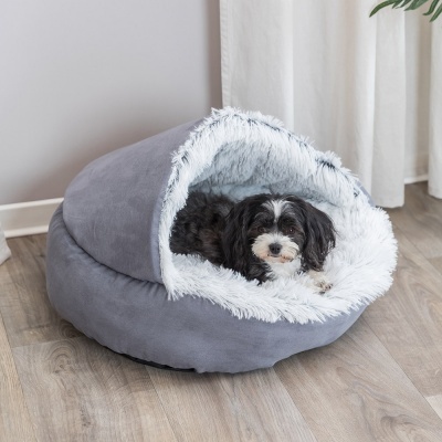 Cama para cão cinzenta com interior felpudo branco, com um cão dentro, em pavimento de madeira.