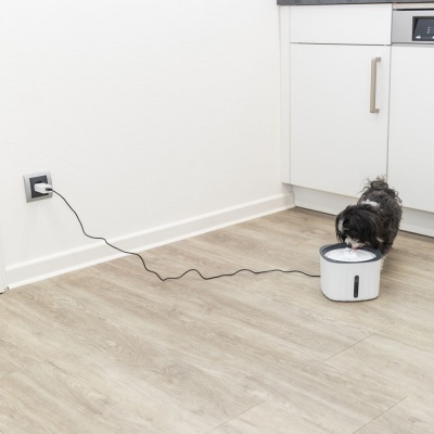 Bebedouro automático branco com base preta num chão de madeira clara com um cão a beber água