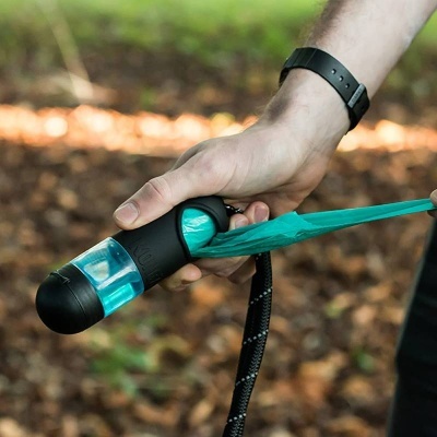 Mão segurando dispensador portátil preto com saco de plástico azul para resíduos de cães
