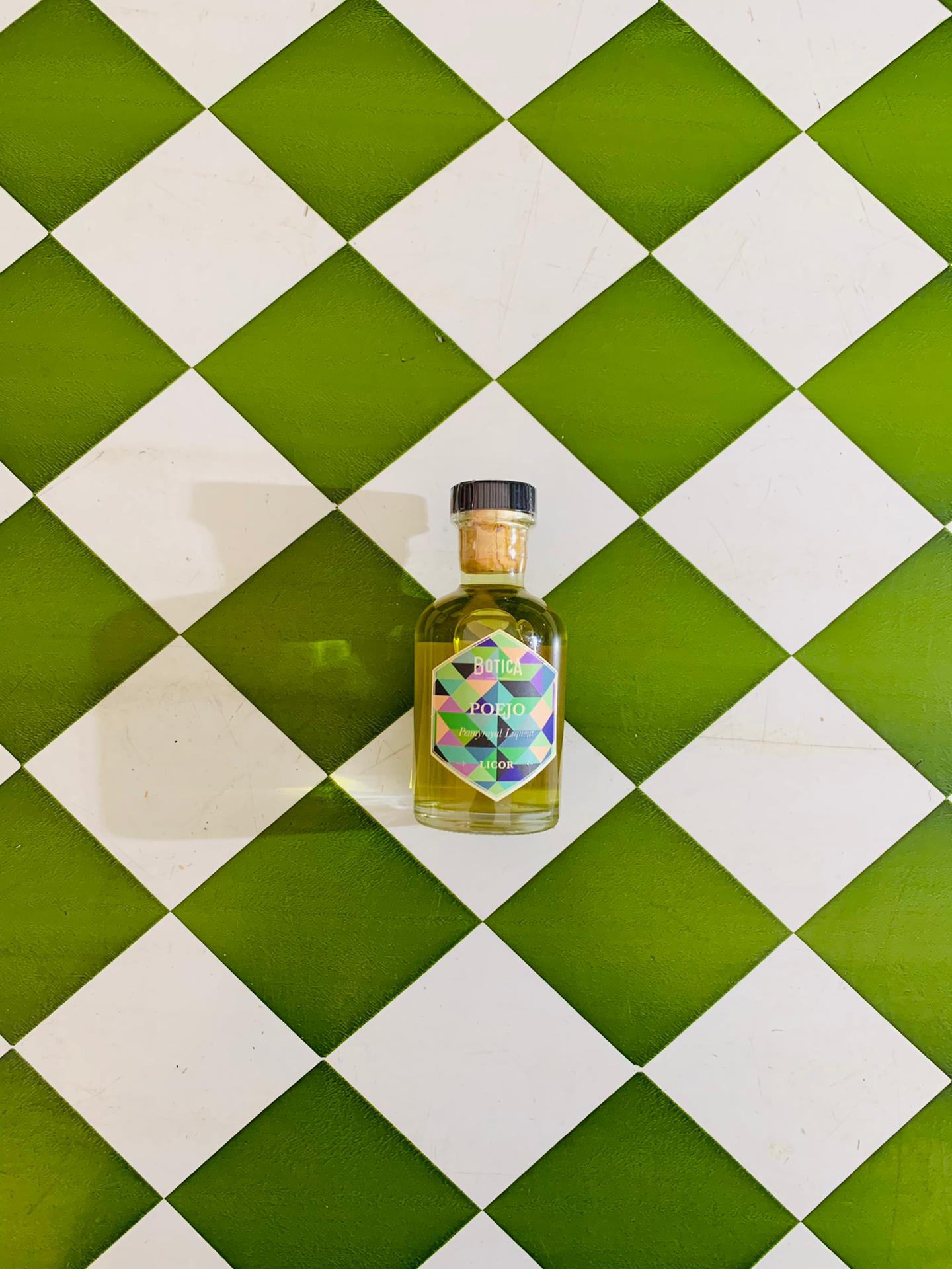 Licor de Poejo 5 cl Frasco de vidro com líquido amarelo e etiqueta colorida sobre azulejos brancos e verdes em xadrez