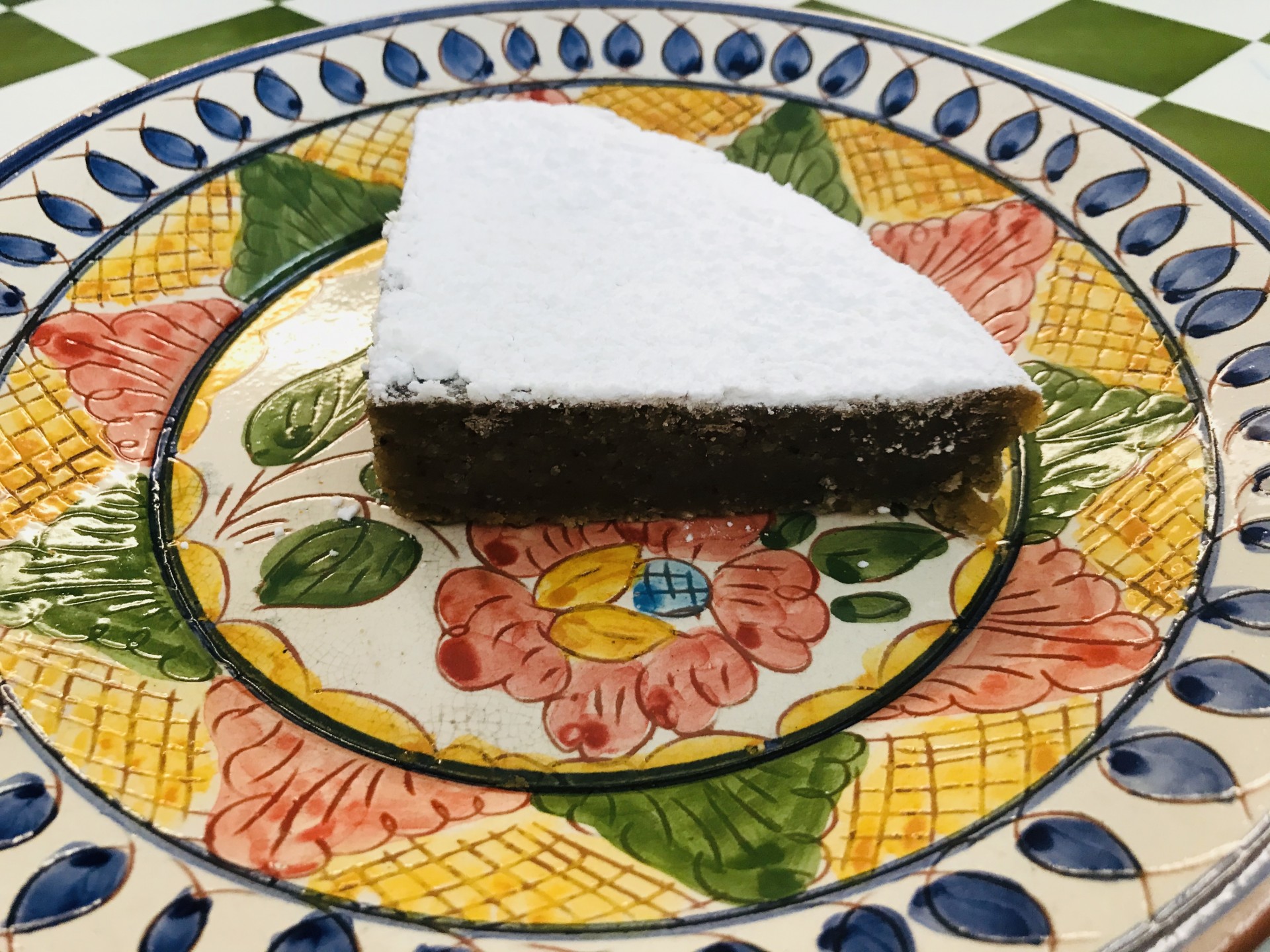 Delícia de Castanha Fatia de bolo com açúcar em pó num prato cerâmico decorado com flores e folhas coloridas