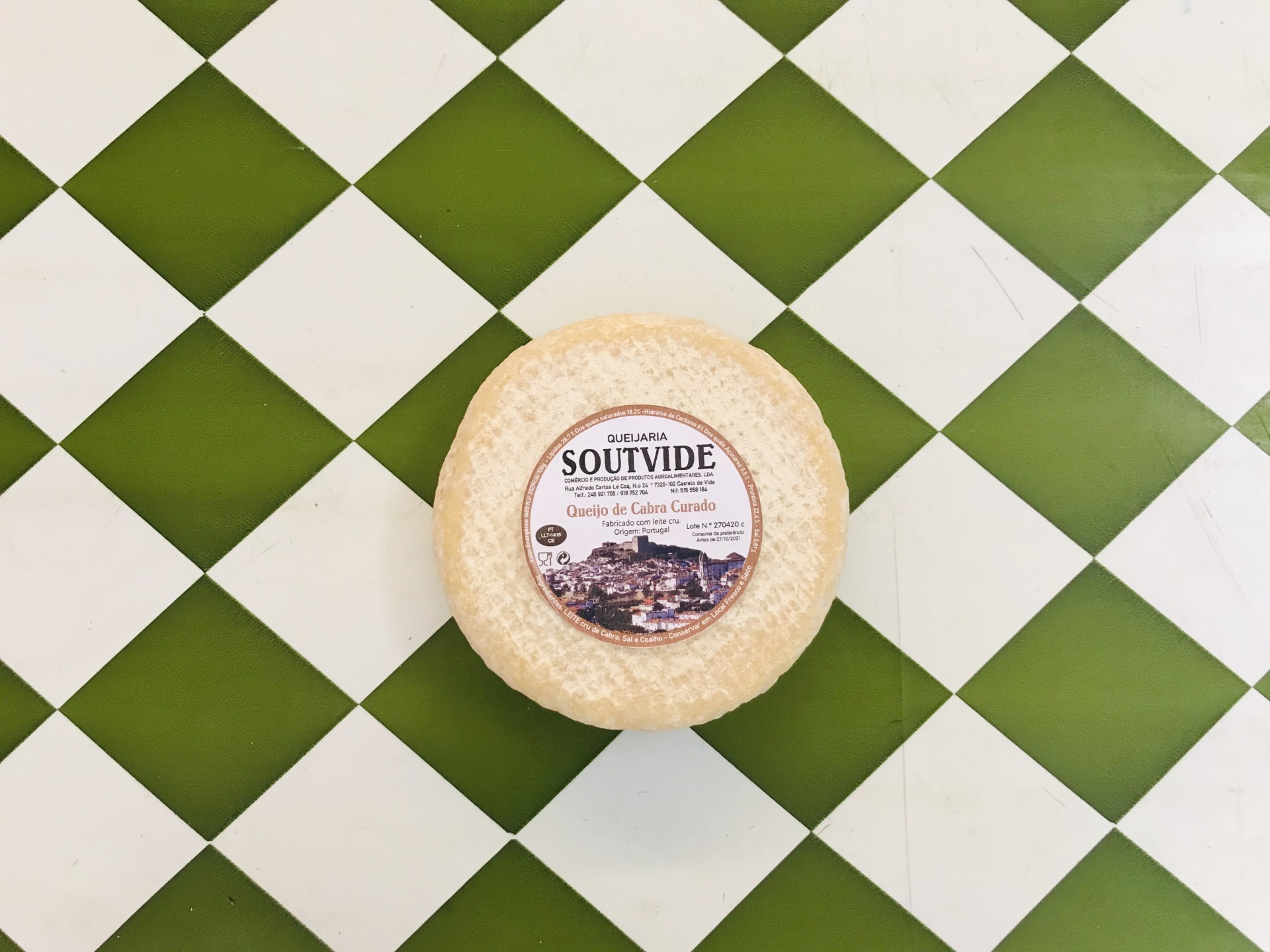 Queijo da Cabra Curado Stv 350gr Queijo redondo com etiqueta na mesa de azulejos verde e branco