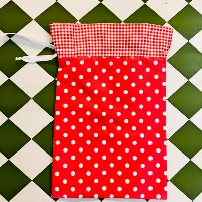 Saco de tecido vermelho com bolinhas brancas e parte superior xadrez vermelho e branco sobre azulejos verdes e brancos