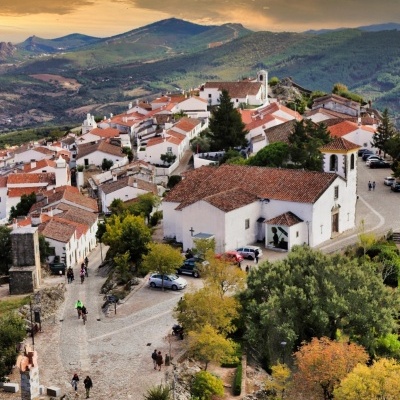 Aldeia pitoresca com casas brancas e telhados vermelhos, estrada de pedra e vegetação