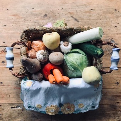 Cesto de vime com legumes variados sobre toalha branca bordada e fundo de madeira