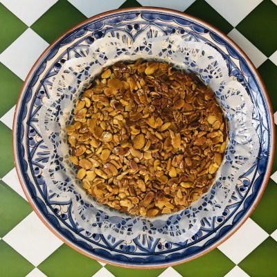 Tarte com amêndoas laminadas num prato azul e branco sobre superfície de losangos verdes e brancos