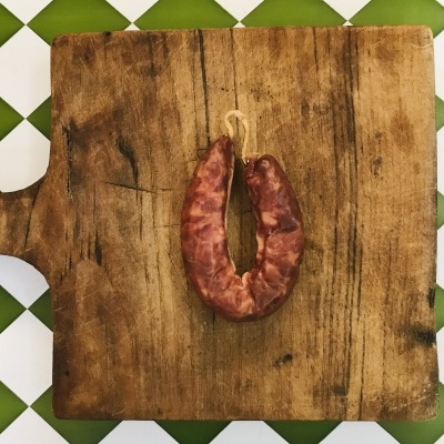 Chouriça pendurada em tábua de madeira sobre azulejos verdes e brancos