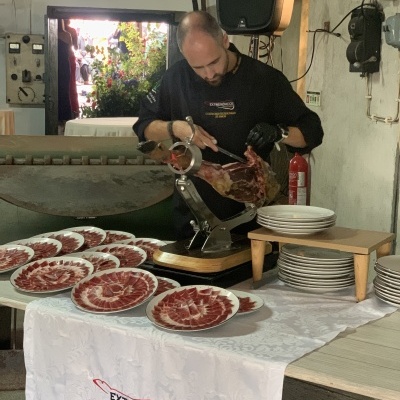 Homem a fatiar presunto ibérico com pratos de presunto sobre mesa com toalha branca
