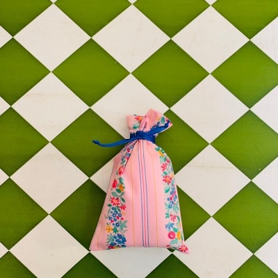 Saquinho de tecido rosa com padrão floral colorido e cordão azul sobre azulejos verde e branco