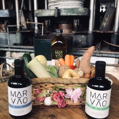 Três garrafas de azeite MAR VÃO com cesta de legumes frescos sobre mesa de madeira em ambiente industrial